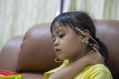 Close-up of cute girl with electrodes on head sitting on sofa at home