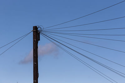 Low angle view of electricity pylon against blue sky