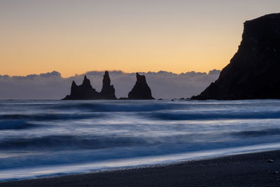 Silhouette rocks on beach against sky during sunset