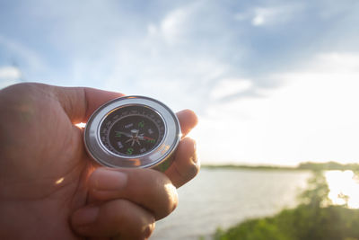 Cropped hand holding navigational compass against sea