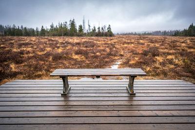 Empty bench in park against sky