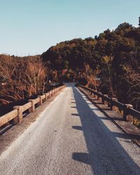 Empty road amidst trees against clear sky