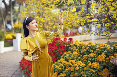 Young woman standing by yellow flowering plants