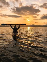 Rear view of silhouette woman kayaking in lake against sky during sunset