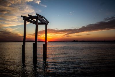 Silhouette hurricane damaged pier and sea against sky during sunset