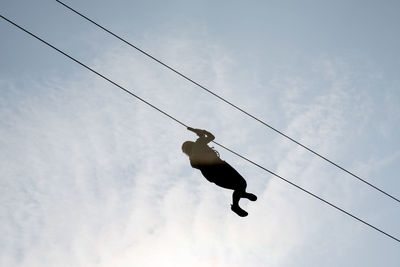 Low angle view of man zip lining against sky