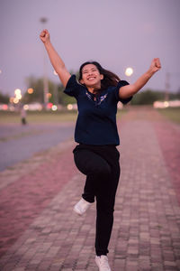 Full length of cheerful young woman dancing on footpath at sunset