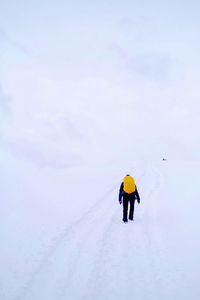 Rear view of person wearing backpack on snow covered field against sky