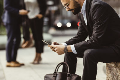 Businessman using smart phone while sitting on seat outdoors