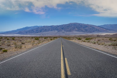 Empty road by mountains against sky