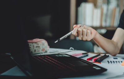 Cropped hand of businesswoman pointing at laptop in office