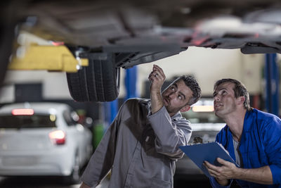 Two car mechanics in a workshop examining car together