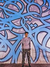 Portrait of young man standing against graffiti wall