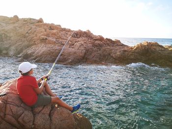 Rear view of man fishing in sea against sky