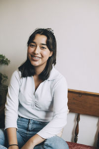 Portrait of smiling teenage girl with braces sitting on sofa against wall at home