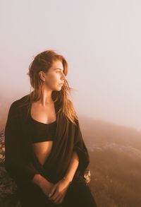 Beautiful young woman looking away against sky