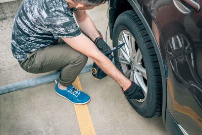 The man sat down near the car and pumps the wheel