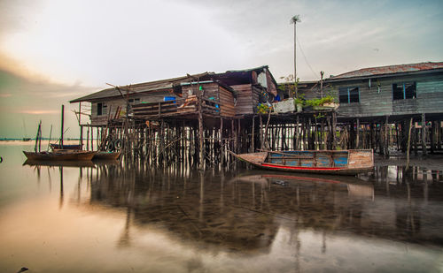 Boats moored by stilt houses in river at sunset