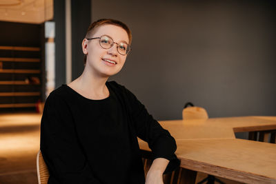 Young woman with short hair in eyeglasses and black sweater sitting at the table in office