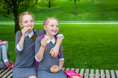 Sisters eating snacks while sitting on seat in park
