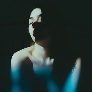 Portrait of young woman standing against dark background