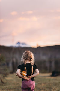 Rear view of girl with stuffed toy standing on field during dusk