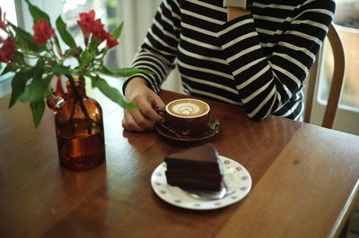 Midsection of woman with coffee cup on table