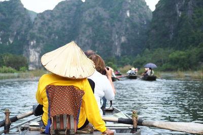 Rear view of tourists sailing on river against mountains
