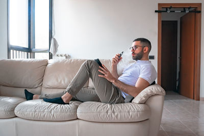 Man smoking while using digital tablet on sofa at home