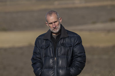 Portrait of adult man in winter clothes standing on fields against blue sky