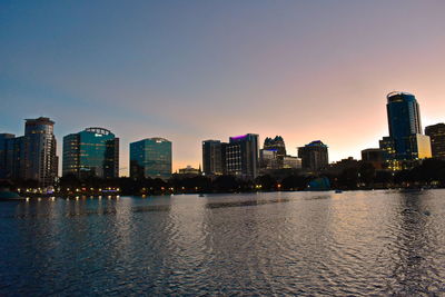 Illuminated buildings in city against clear sky during sunset