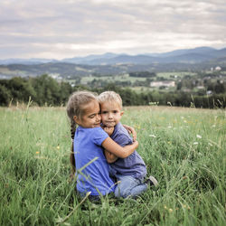 Cute sibling embracing on grassy field