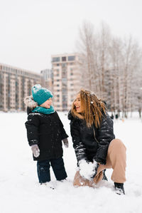 Mother and child are playing in the snow. woman is holding a snowball. scene is joyful and playful