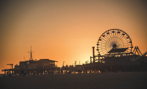 Silhouette ferris wheel on beach against clear sky during sunset