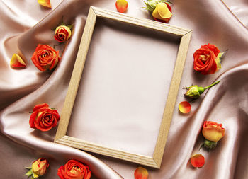 Flowers composition. wooden frame and red roses and leaves on beige silk background. 