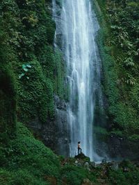 Shirtless man standing on rock against waterfall