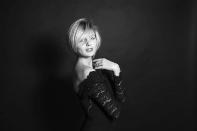 Portrait of young woman standing against black background