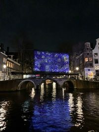 Illuminated bridge over river in city at night