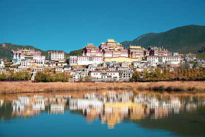 Reflection of buildings in lake against clear blue sky