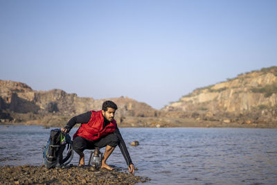 Full length of man sitting on lake against sky