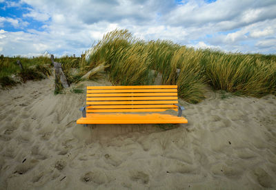 Empty seats on sand at beach against sky