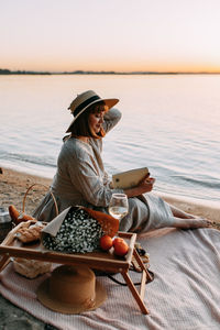 Woman sitting by lake against sky during sunset