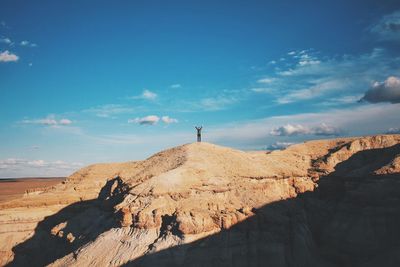 Young man with arms raised standing on top of mountain during sunny day