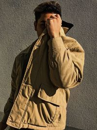 Man covering face with jacket while standing with umbrella