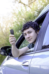 Portrait of young man looking through car window while holding key