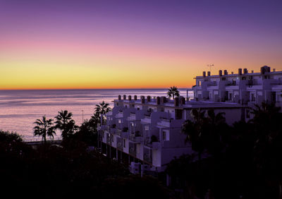 Scenic view of sea against buildings at sunset