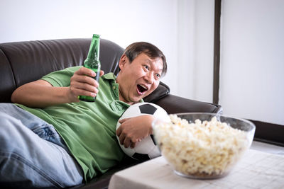 Mature man watching sport while lying on sofa at home