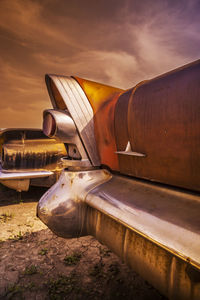 Rusty machine on field against sky during sunset