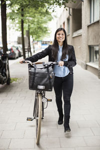 Full length portrait of happy businesswoman with bicycle walking on sidewalk