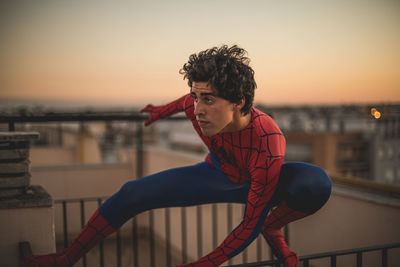 Young man in costume on railing on terrace during sunset